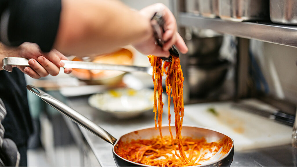 Young male chef making Bolognese pasta in a commercial kitchen. Close-up.